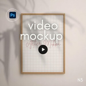 Puede incluir: Un marco de madera rectangular que contiene un fondo con patrón de cuadrícula blanca con el texto video mockup y Atelier Mikka en fuente cursiva. Un icono de botón de reproducción circular negro está centrado en la cuadrícula sobre una pared.
