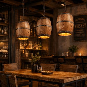 May include: Three pendant lights shaped like wooden whiskey barrels, each featuring dark metal bands with visible rivets. The barrels are suspended by chains from the ceiling, with warm light emitting from the open bottom of each fixture.