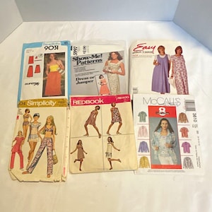 May include: A collection of six vintage sewing patterns from brands including Simplicity, Show-Me! Patterns, Easy Stitch 'n Save, Redbook, and McCall's. Each paper envelope features illustrations of various clothing styles, including dresses, jumpers, and pantsuits, with printed text and model imagery.