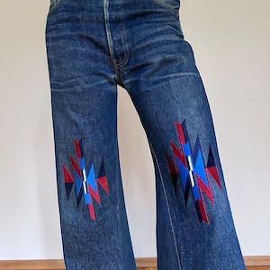 May include: Blue denim flared jeans with red, blue, and white geometric embroidery on the knees.