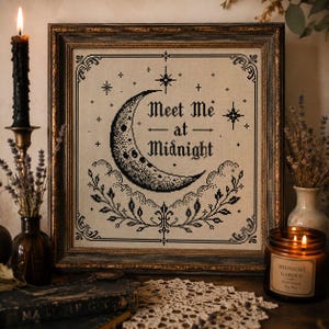 以下が含まれることがあります： 三日月と「Meet Me at Midnight」の文字が黒で刺繍された額入りのクロスステッチ。 作品はクリーム色の背景にあり、暗く装飾的なフレームに入っています。 ろうそくの火とドライフラワーが入った小さな花瓶も写っています。