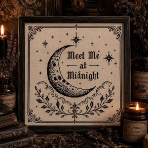 Könnte beinhalten: Ein quadratisch gerahmtes Kreuzstich-Stickbild auf beigem Stoff mit einem schwarzen Halbmond, Sternen und dekorativem Blattwerk. Der Text "Meet Me at Midnight" ist mittig platziert und von einem detaillierten schwarzen Rahmen umgeben.