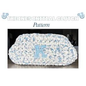 May include: A crochet clutch bag featuring a white and blue floral pattern with a central light blue and white gingham letter K appliqué. The text THE INES INITIAL CLUTCH Pattern is displayed above the bag in a bold, white, outlined font.