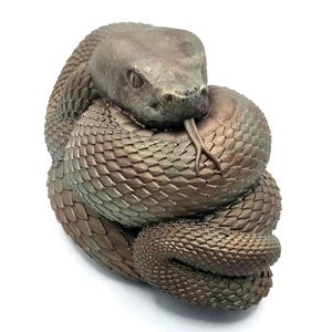 May include: A coiled bronze-coloured snake figurine with detailed scales and a forked tongue. The snake's head is raised, and its eyes are visible. The figurine is set against a white background.