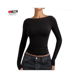 May include: A long-sleeved black top with a wide boat neckline and a fitted silhouette. The garment features a smooth, solid black fabric that extends to the wrists and sits at the waist, paired with dark charcoal denim jeans with a button fly.