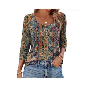 Puede incluir: Una blusa de manga larga con un vibrante estampado floral y de cachemira multicolor en tonos turquesa, dorado y rojo intenso. La prenda tiene un cuello redondo con una fila vertical de cuatro botones blancos pequeños y se combina con jeans azules.