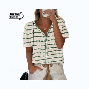 May include: Cream-colored, short-sleeved cardigan with horizontal green stripes. The button-down shirt has a V-neck and green trim. The image also includes the text "FREE DELIVERY" in a black box with a white arrow.