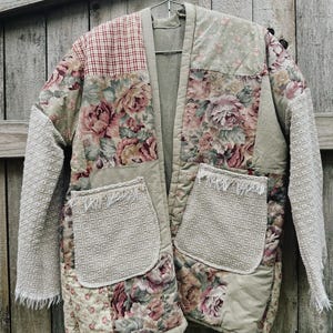 May include: A quilted jacket featuring a patchwork design of floral patterns, red and white gingham, and solid beige fabric. The garment includes two large front pockets with frayed edges and long sleeves made of a textured, off-white fabric.