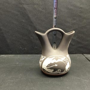 May include: A matte grey ceramic wedding vase with a double-spout design and a central handle. The body features a white graphic of a bear and geometric patterns. A vertical measuring tape shows the vase stands approximately 7 inches in height.