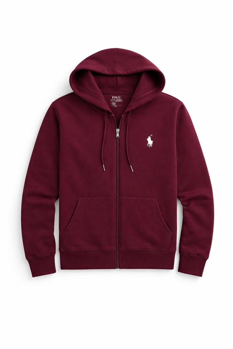 May include: A burgundy zip-up hoodie with a drawstring hood and front pockets. The hoodie features a white embroidered polo player logo on the left chest. The zipper is silver. The garment is made of a soft, comfortable material.