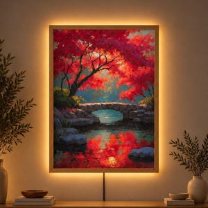 Puede incluir: Una pieza de arte mural rectangular que presenta una pintura de un puente de piedra sobre un cuerpo de agua tranquilo, rodeado de árboles frondosos con follaje rojo brillante. La obra está enmarcada en madera e iluminada por luz LED.