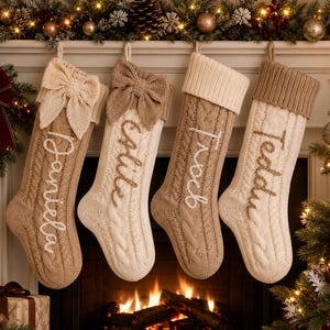 Peut inclure: Quatre chaussettes de Noël en tricot torsadé suspendues en rangée. Les chaussettes sont beiges et crème, chacune ornée d'un grand nœud en tricot sur le dessus et d'un prénom brodé en écriture cursive : Daniela, Callie, Jacob et Teddy.