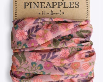 Puede incluir: Diadema floral con fondo rosa y variedad de flores rosas, naranjas y verdes. La diadema está empaquetada en un cartón con el texto "The Curly Pineapples Headband".