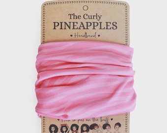 Puede incluir: Una diadema rosa y blanca a rayas de "The Curly Pineapples" se muestra sobre un respaldo de cartón marrón. El texto "The Curly Pineapples" y "Headband" están impresos en la tarjeta. La diadema está enrollada.