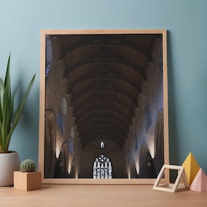 May include: A framed print of a cathedral interior. The image showcases a long, arched ceiling with stone walls and a stained-glass window at the far end. The print is in a light-colored wooden frame, resting on a wooden surface.