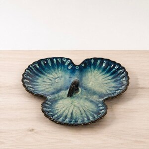 May include: A three-section ceramic serving dish with a scalloped shell-like shape and a central handle. The glaze features a gradient of deep navy blue at the edges transitioning into a lighter, mottled seafoam green toward the center of each section.