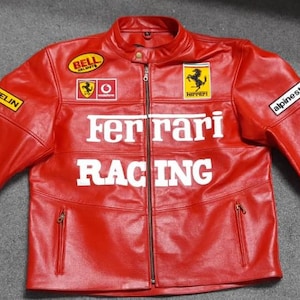 May include: A bright red leather racing jacket featuring a front zipper closure, two zippered pockets, and white text reading Ferrari Racing. The jacket includes various sponsor patches such as Bell, Michelin, Alpinestars, and the Ferrari logo.