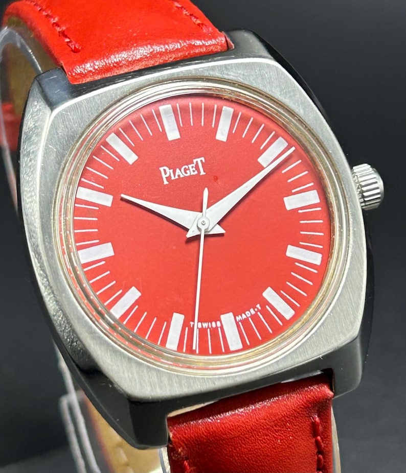 Puede incluir: Un reloj de pulsera con esfera roja brillante y caja de metal plateado cepillado. La esfera presenta marcadores de hora blancos, manecillas plateadas y el texto Piaget y Swiss Made-T. El reloj est&aacute; sujeto a una correa de cuero roja con costuras.