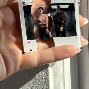May include: A clear acrylic keychain shaped like two interlocking Instagram post frames. The left frame shows a shirtless person with tattoos, while the right frame displays a person in a dark jacket. Both frames feature the Instagram interface.