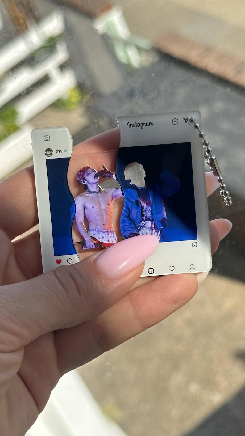 May include: A two-piece acrylic keychain shaped like an Instagram post interface. The white frame features the text Instagram, thv, and social media icons. The center displays a split image of a person in a blue jacket and a shirtless person.