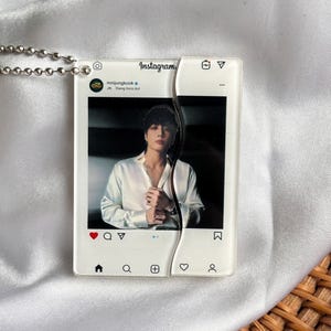 May include: A clear acrylic pendant with a silver chain, featuring a photo of a person in a white shirt, styled as an Instagram post. The pendant is split in two pieces. The Instagram logo and icons are visible.