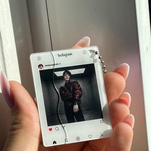 May include: A rectangular acrylic keychain featuring a printed Instagram interface design. The display shows the username mnijungkook and a photograph of a person in a dark leather jacket. A silver ball chain is attached to the top right corner.