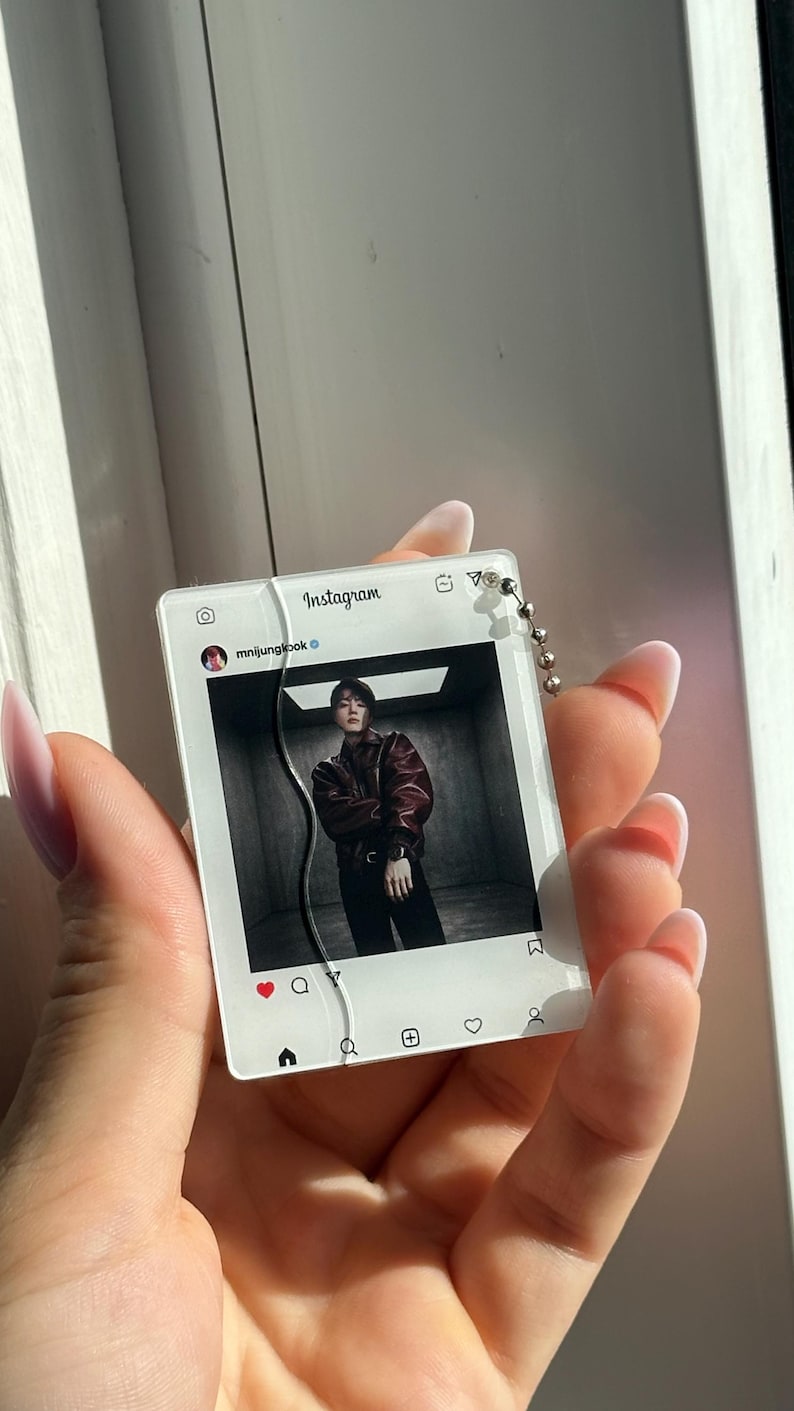 May include: A rectangular acrylic keychain featuring a printed Instagram interface design. The display shows the username mnijungkook and a photograph of a person in a dark leather jacket. A silver ball chain is attached to the top right corner.