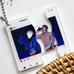 May include: A clear acrylic pendant shaped like an Instagram post interface, featuring a split design with a metal ball chain. The graphic displays a person wearing a red bandana and a blue jacket, with the username thv and Instagram icons visible.