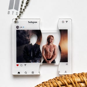 May include: A clear acrylic keychain shaped like a puzzle piece featuring an Instagram post interface. The design displays a profile photo of j.m, a dark jacket, and a shirtless person with light hair. It includes a silver ball chain and BTS logo.