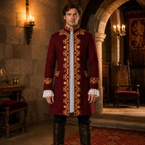 May include: A deep red long coat featuring intricate gold embroidery along the front opening, collar, and cuffs. The coat is worn over a white shirt with visible lace-trimmed cuffs, paired with dark trousers and tall brown leather boots.