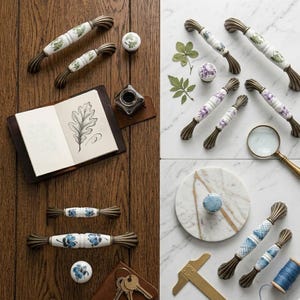 May include: A collection of ceramic cabinet hardware featuring white handles and knobs with floral and geometric patterns, accented by antique brass-toned metal ends. The set includes various sizes of drawer pulls and round knobs displayed alongside a sketchbook with a leaf drawing, an inkwell, a magnifying glass, and a brass tool.