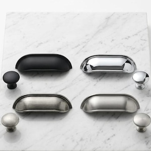 May include: A collection of four metal cup pulls and four matching round knobs in various finishes including matte black, polished chrome, brushed nickel, and satin nickel, arranged in a grid pattern on a white marble surface.