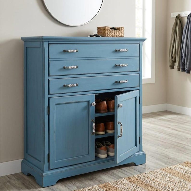 May include: A blue wooden storage cabinet featuring three horizontal drawers with decorative white and black patterned knobs, and two doors that open to reveal interior shelving containing several pairs of brown and gray casual shoes.