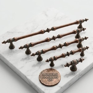 May include: A collection of five copper-toned metal cabinet pulls and one circular knob, each featuring a textured, spindle-like design with decorative finials. A round copper medallion is embossed with the text MODERN HANDLES CO.