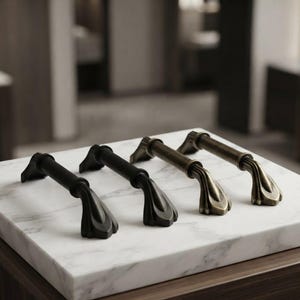 May include: Two matte black metal drawer pulls and two antique brass metal drawer pulls. Each pull features a horizontal bar with flared, petal-like mounting ends. The hardware is arranged in a row, showcasing the contrasting dark and metallic finishes.