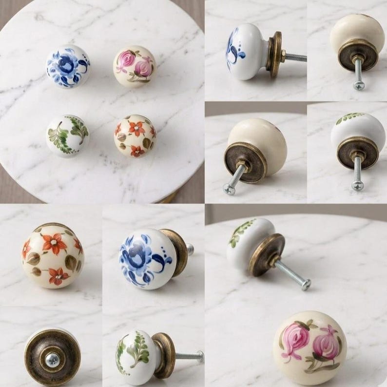 May include: A collection of round ceramic cabinet knobs featuring hand-painted floral designs in blue, pink, green, and orange. Each knob has a smooth, off-white base and is attached to a metallic bronze-toned hardware screw for mounting.