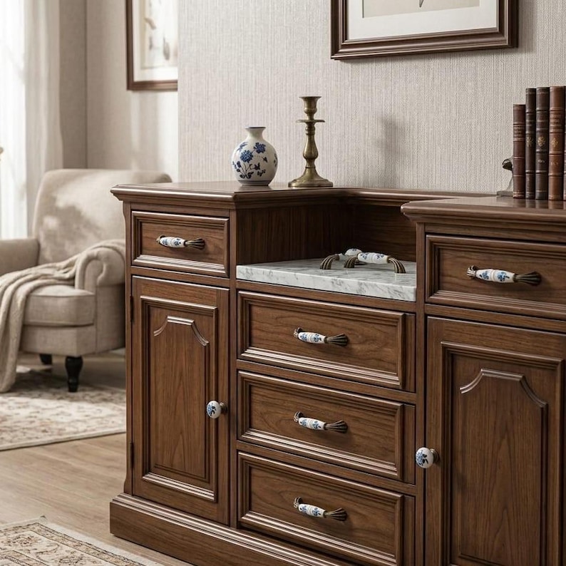 May include: A dark wood sideboard featuring a white marble countertop, three central drawers, and two side cabinets. Each drawer and cabinet door is fitted with white ceramic handles decorated with blue floral patterns and brass-toned accents.