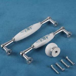 May include: Two chrome-plated metal drawer pulls with white ceramic centers featuring a blue floral pattern, one round white ceramic knob with a chrome base, and four silver-colored metal mounting screws for cabinet hardware installation.