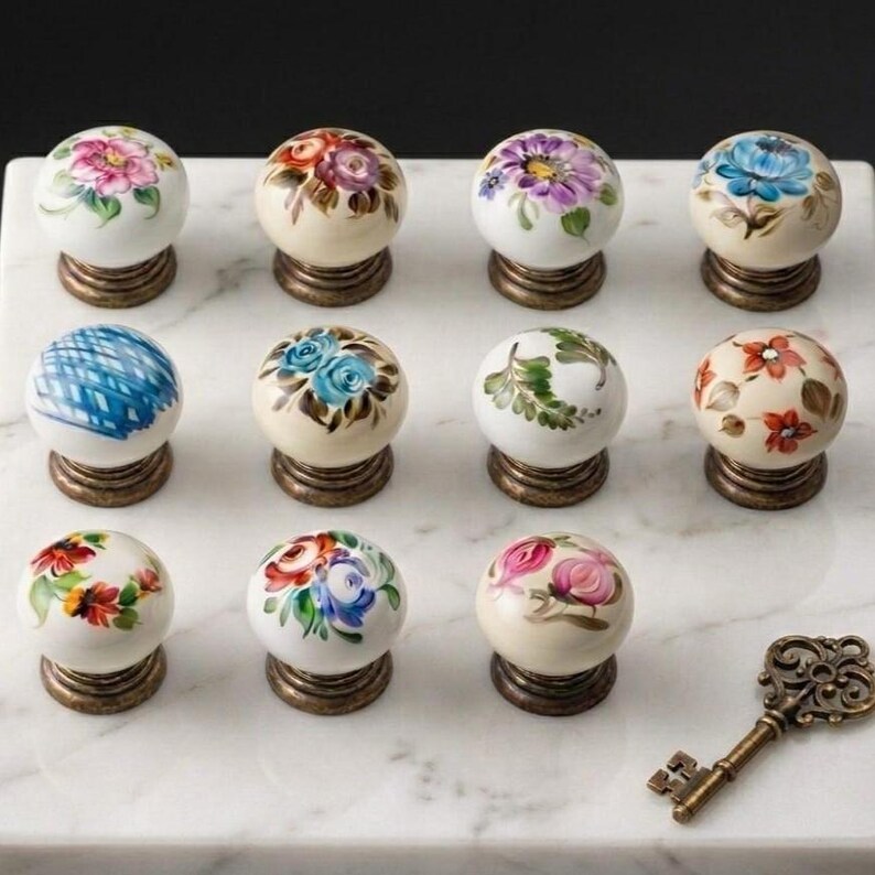 May include: A collection of eleven round ceramic cabinet knobs featuring various hand-painted floral and geometric patterns in multiple colors, each mounted on a metallic base, accompanied by a single ornate antique-style metal skeleton key.