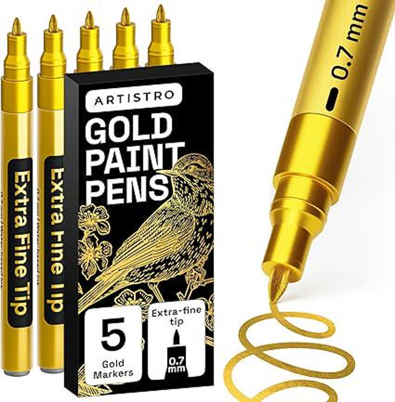 May include: Gold paint pens with extra fine tips. The black box features the text "ARTISTRO GOLD PAINT PENS" and a gold illustration of a bird. The box indicates that it contains 5 gold markers with 0.7 mm tips. The pens are gold.