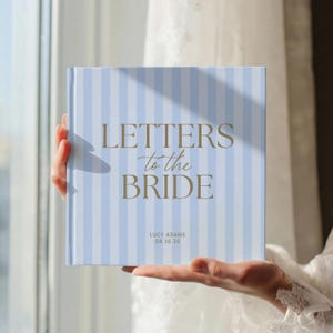 Pode incluir: Um livro de capa dura quadrado com uma capa de listras verticais azul-claras e brancas. O texto "LETTERS to the BRIDE" está impresso em dourado no centro, com "LUCY ADAMS" e "08 16 26" em letras douradas menores abaixo do título.