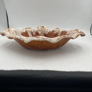 Puede incluir: Un cuenco de cerámica poco profundo con una base de textura de grano de madera marrón y un borde festoneado y ondulado. Los bordes del borde están acabados con un esmalte blanco estilo goteo que contrasta con el cuerpo marrón, creando un borde decorativo.