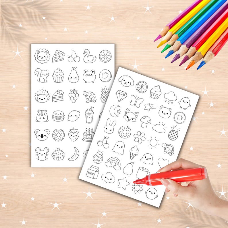May include: Two white rectangular sheets featuring black line art illustrations of various small icons including animals, food items, celestial shapes, and plants. A red marker is positioned on one sheet, and a set of colored pencils is nearby.