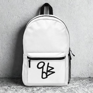 Könnte beinhalten: Weißer Rucksack mit schwarzem Tragegriff, Reißverschluss und seitlicher Netztasche. Die Vordertasche hat ein schwarzes Grafikdesign. Der Rucksack besteht aus strapazierfähigem Material und eignet sich zum Tragen von Büchern, Laptops und anderen wichtigen Dingen.