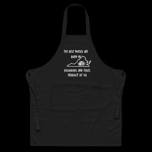 May include: Black apron with a front pocket and neck strap. The apron features white text that reads "THE BEST NURSES ARE BORN IN" above a Virginia state outline with a nurse's cap and a cigarette. Below the state outline, the text reads "DOGWOODS AND TAXES PRODUCT OF VA."