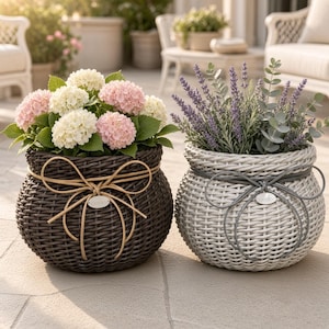 May include: Two round woven planters with decorative bows and small oval tags labelled GARDEN. The dark brown planter holds white and pink hydrangea flowers with green leaves. The light grey planter contains purple lavender and green eucalyptus stems.