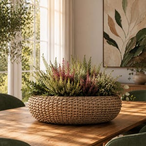 May include: A round, woven seagrass basket filled with a dense arrangement of heather plants. The heather features a mix of vibrant magenta, soft pink, and creamy white flower spikes interspersed with fine, needle-like green foliage.