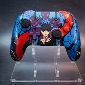 May include: Custom-painted video game controller with a striking design. The controller features a blue, red, and purple color scheme with a detailed anime-style illustration. The design includes a character with a finger to their lips, and a cross-shaped button.