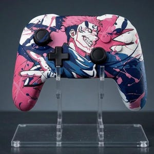 May include: A custom video game controller featuring a vibrant anime-style design. The controller has a pink, blue, and white color scheme with an illustration of a character. The controller is displayed on a clear acrylic stand.