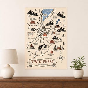 May include: A cream-colored map print of Twin Peaks, Washington, featuring black ink illustrations of mountains, forests, and roads. The map includes labeled landmarks like Pearl Lake, the Great Northern Hotel, and the Log Lady's Cabin in red ink.